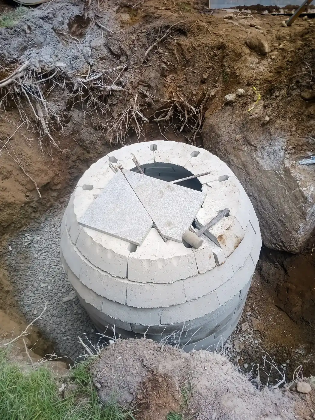 Trench with perforated drain pipe and crushed stone running along the edge of a backyard lawn
