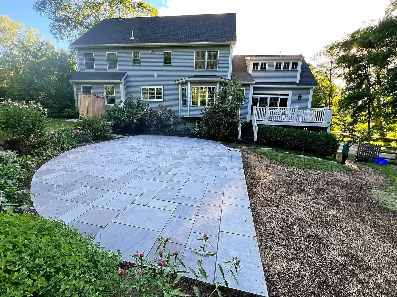 Large bluestone patio behind a colonial style home with a level lawn and planting beds