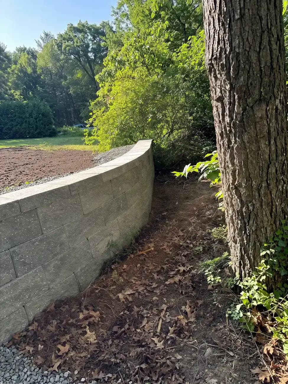 Curved segmental block retaining wall holding back a sloped lawn beside a residential driveway