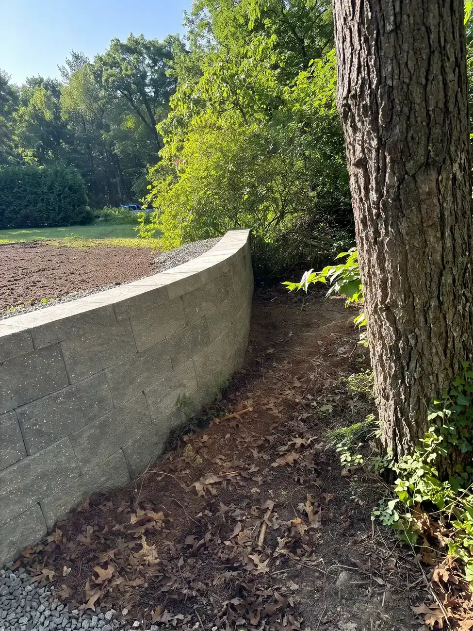 Curved block retaining wall on a wooded lot, a Machado Landscaping project