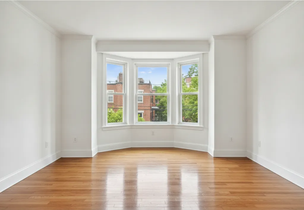 Clean, empty room with bright hardwood floors and bay windows after construction